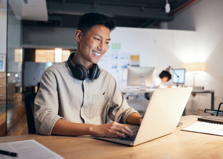 Smiling man on a laptop working at an office desk